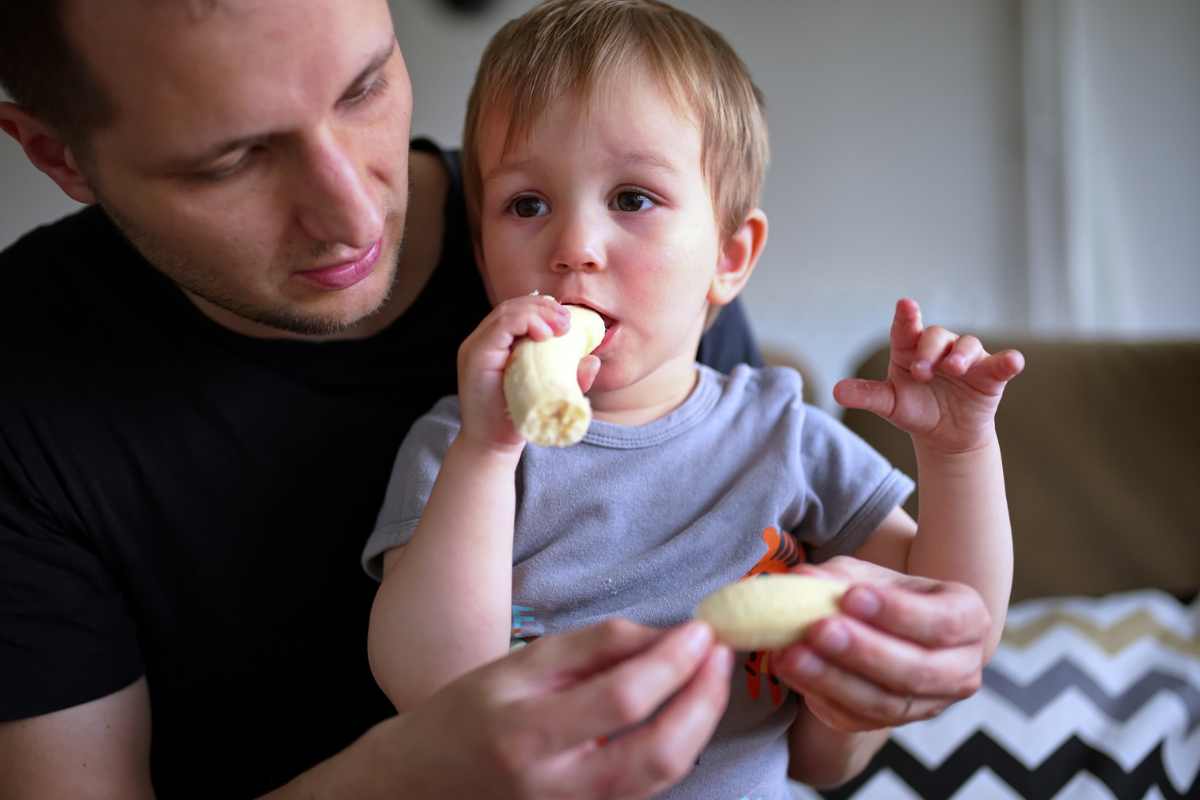 bambino mangia banana tra le braccia del padre